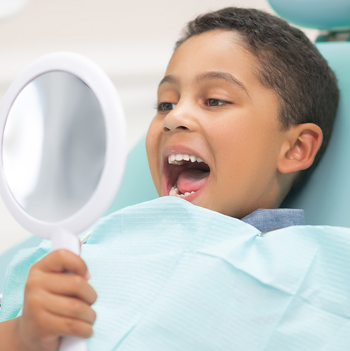 child at the dentist looking at teeth in mirror